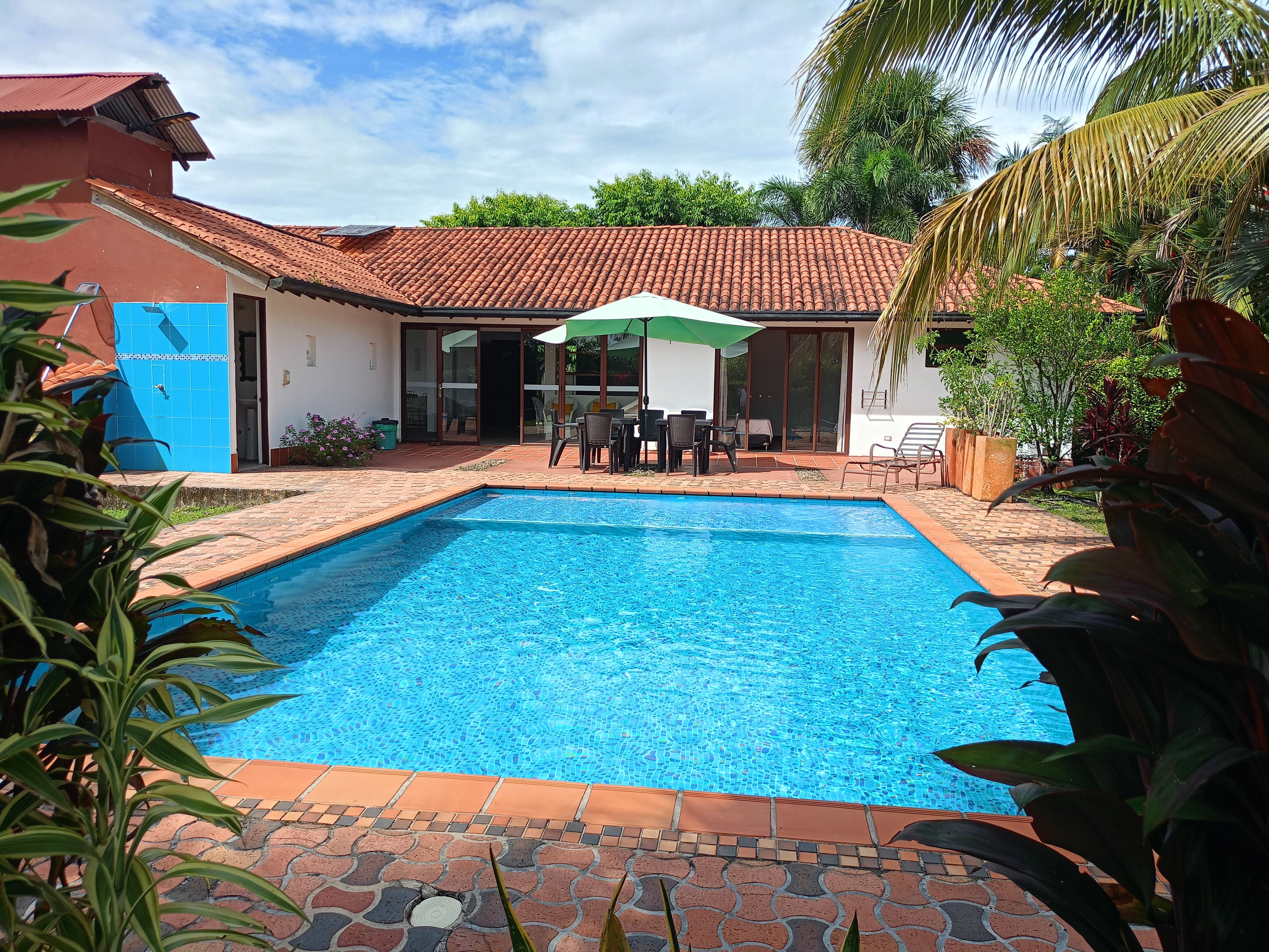A rectangular swimming pool with a tiled deck, surrounded by a patio area with outdoor furniture and a covered seating area.