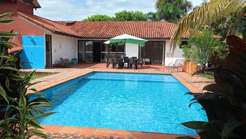 A rectangular swimming pool with a tiled deck, surrounded by a patio area with outdoor furniture and a covered seating area.