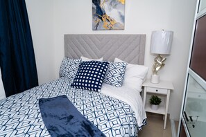 A modern bedroom with a geometric patterned bedspread, a tufted headboard, and a bedside lamp. - New Listing (San Juan)