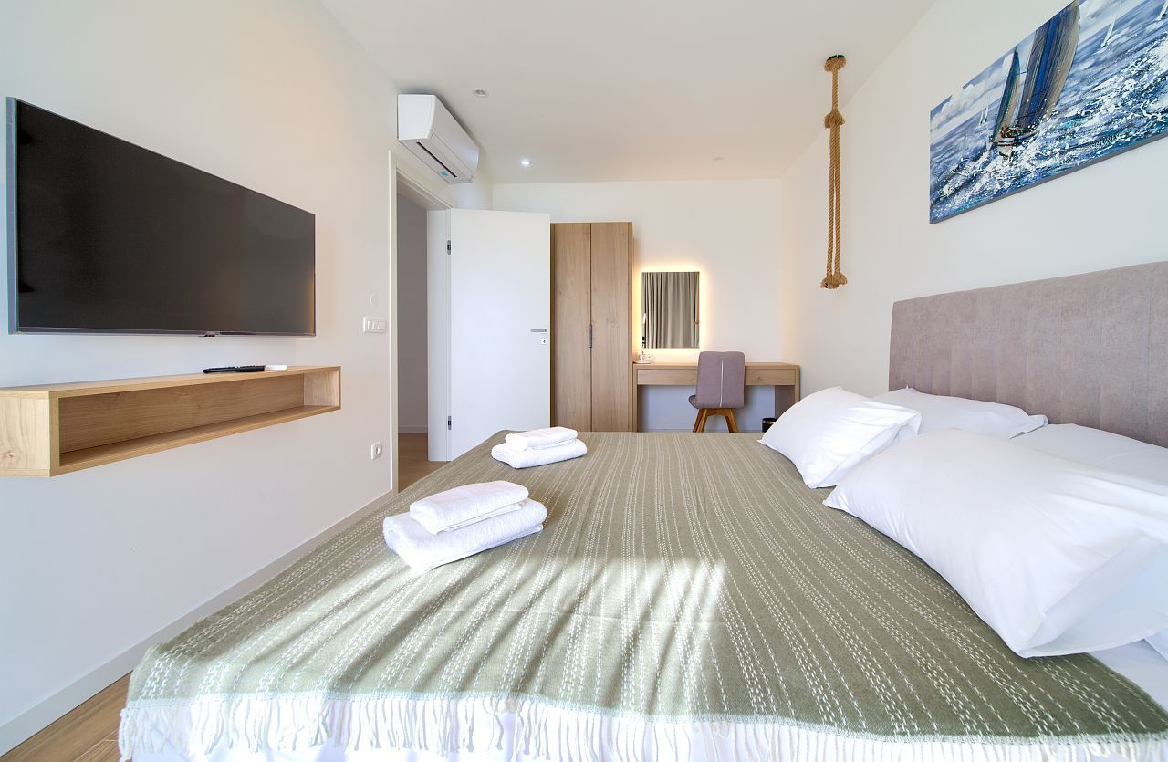 A hotel room with a large bed, a flat-screen TV mounted on the wall, a desk with a chair, and a painting on the wall.