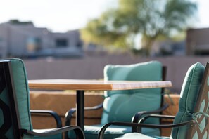 Eine Terrasse mit Tisch und Stühlen, im Hintergrund ein Gebäude und ein Baum.