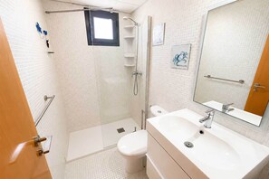 Et badeværelse med bruser, toilet og håndvask, med fliserede vægge og et spejl.