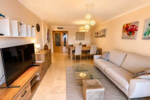 A modern living room with a flat-screen TV, sofa, coffee table, and dining area. - Apartment with Terrace and Sea Views in Casares (Casares)