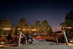 An outdoor seating area with tables and chairs, surrounded by trees and string lights.