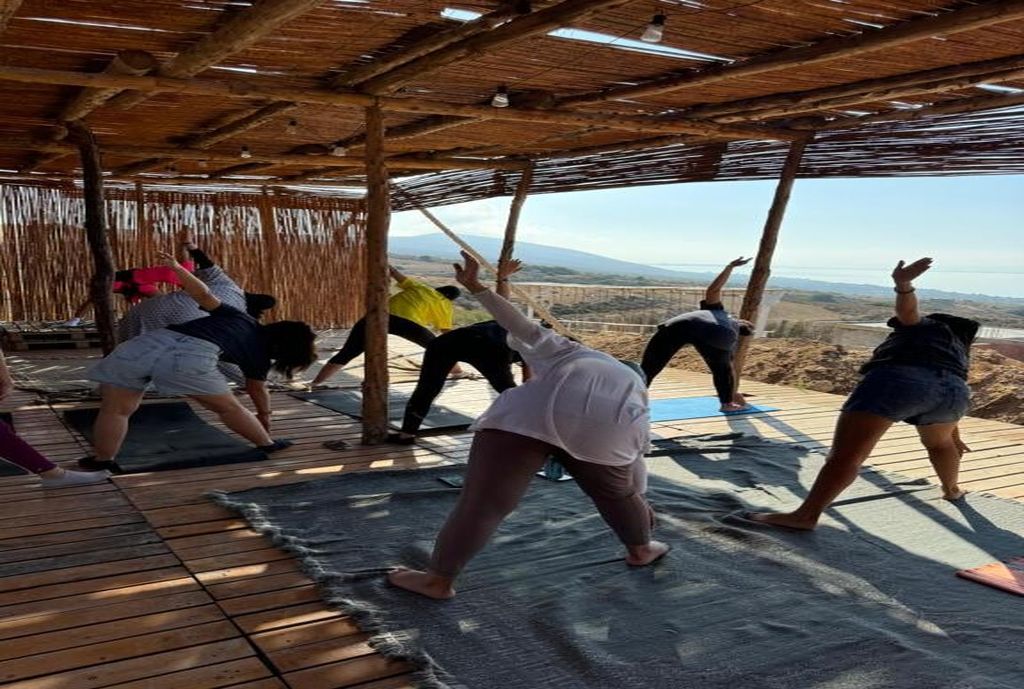 A group of people performing yoga on mats under a wooden structure with a view of a landscape.