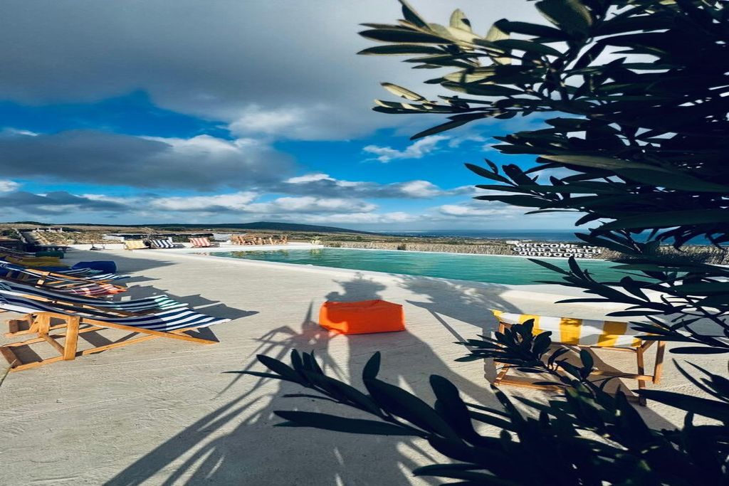 A poolside area with lounge chairs and a small orange seating area, overlooking a beach and the sea.