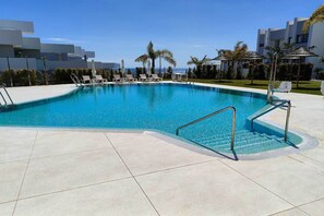 A swimming pool with a tiled deck, lounge chairs, and palm trees. - Apartment 'Pure South' with Mediterranean Views (San Luis De Sabinillas)