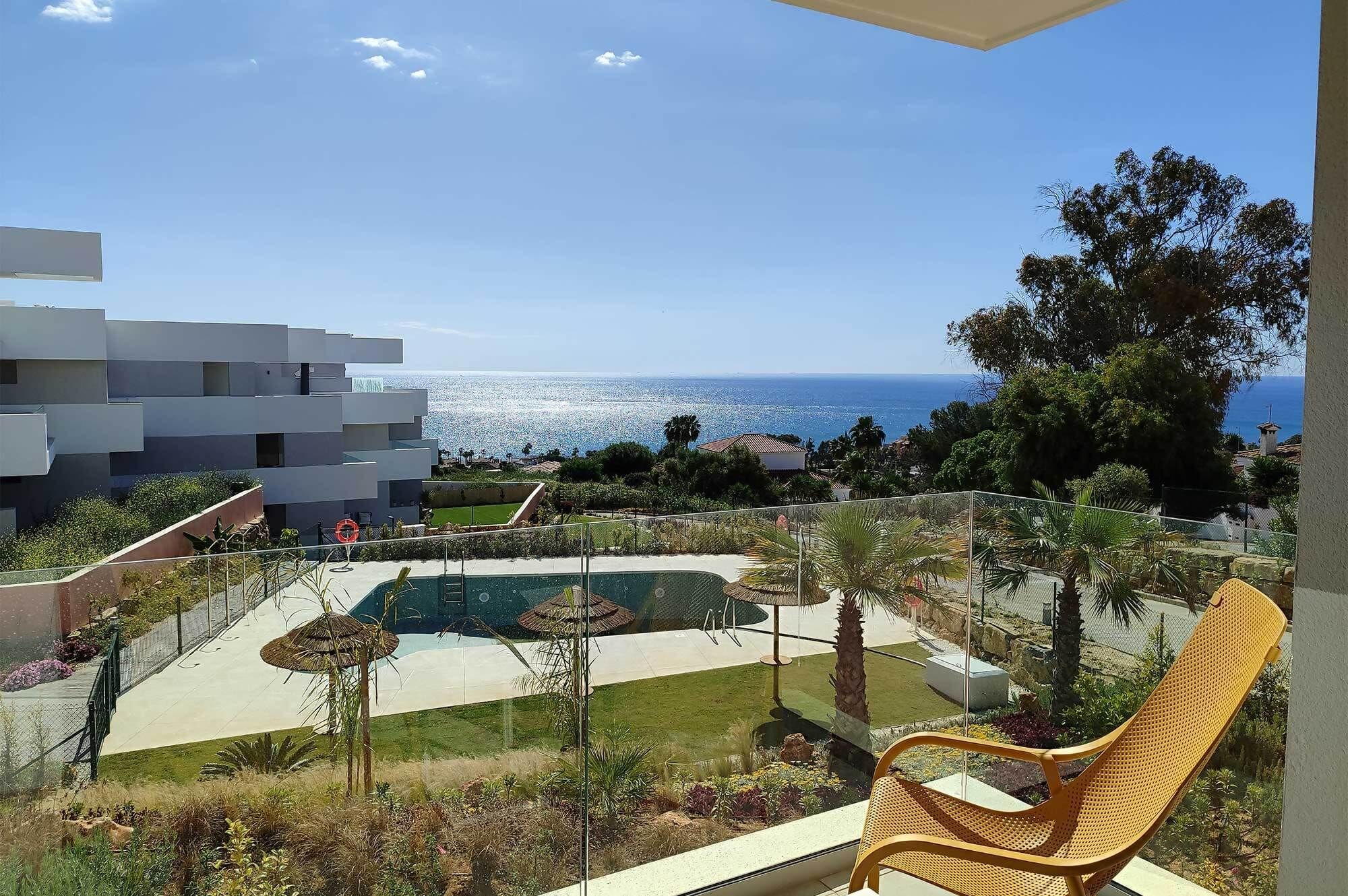 A balcony with a view of a swimming pool, a modern building, and a clear sky.