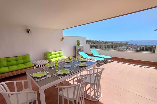 Un balcón con una mesa de comedor para cuatro personas, un sofá y dos sillones.