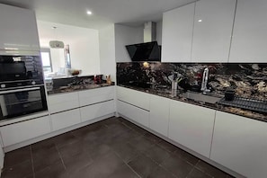 A modern kitchen with white cabinets, a black marble backsplash, and a stainless steel sink. - Apartment with Sea and Doña Julia Golf Course View (Casares)