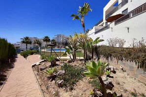 A pathway leading to a pool area with palm trees and a white building in the background. - Apartment with Sea and Doña Julia Golf Course View (Casares)