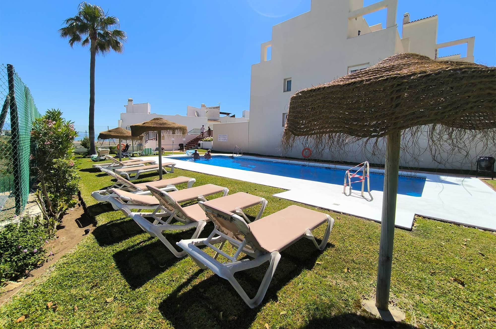 A pool area with lounge chairs and a thatched umbrella.