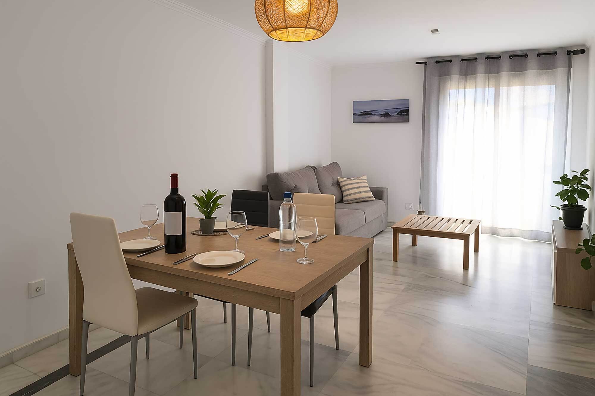 Un comedor con una mesa de madera dispuesta para cuatro, una botella de vino y una planta en maceta.