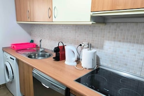 A kitchen with a sink, a kettle, a toaster, a dish rack, and a washing machine. - Bright Apartment in Estrella de la Bahía (Casares)