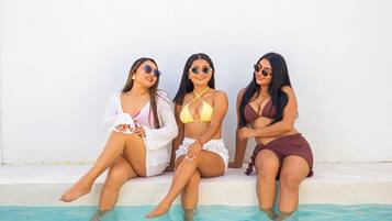 Três pessoas sentadas à beira de uma piscina, com uma parede branca e lisa ao fundo.