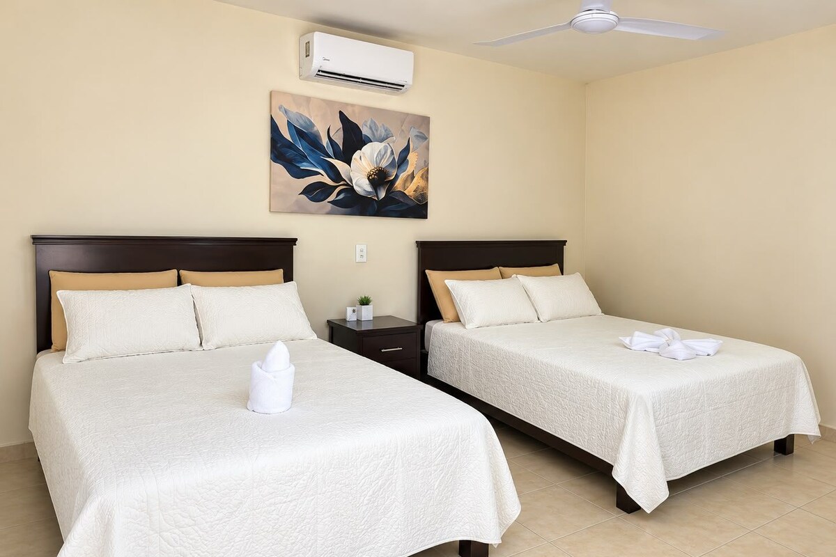 A hotel room with two beds, beige walls, a ceiling fan, and a painting.