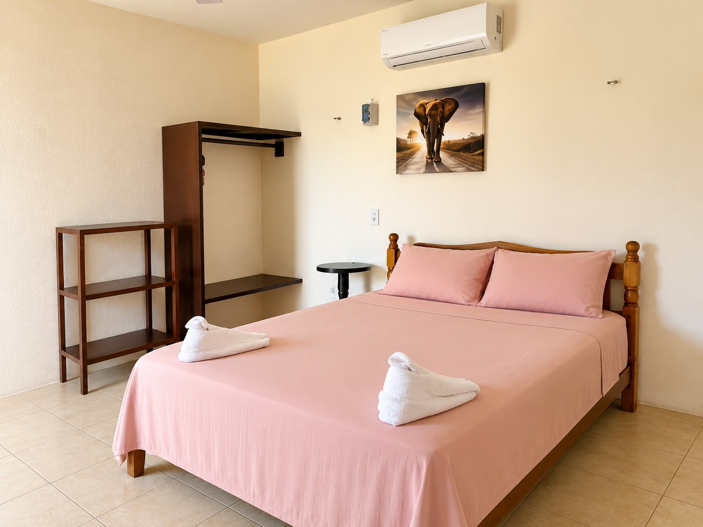 Quarto de hotel com cama, guarda-roupa de madeira, uma mesinha e ar condicionado.