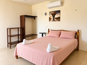 Habitación de hotel con cama, armario de madera, una mesita y un equipo de aire acondicionado.
