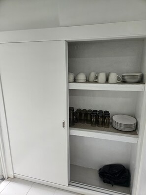 A white wardrobe with open doors revealing shelves with kitchenware.