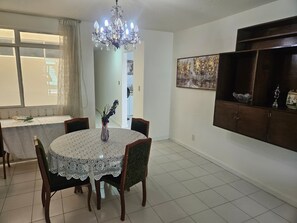 Un coin repas comprenant une table ronde, des chaises, un lustre, une fenêtre avec des rideaux et un meuble mural agrémenté d’objets décoratifs.