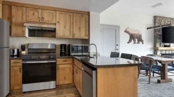 A modern kitchen with wooden cabinets, stainless steel appliances, and a dining area with a stone fireplace. - Heavenly! South Lake Tahoe for Thanksgiving weekend and beyond. (South Lake Tahoe)