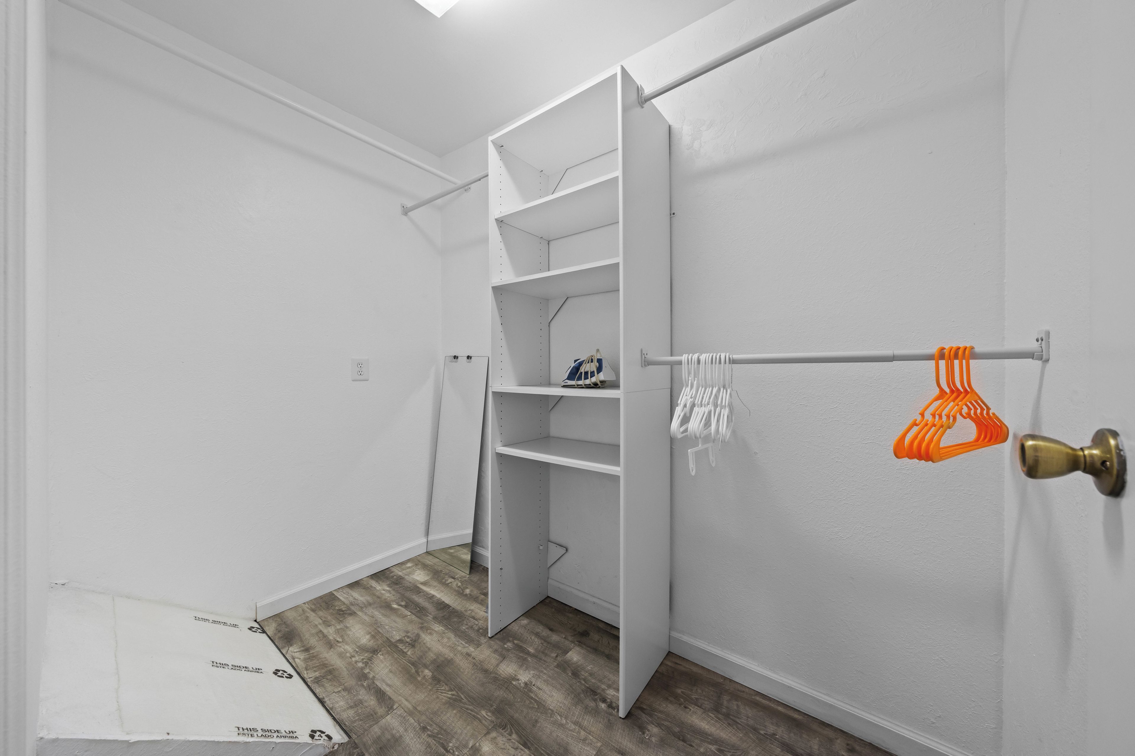 A room with a white closet, a wooden floor, and a door with an orange towel rack.