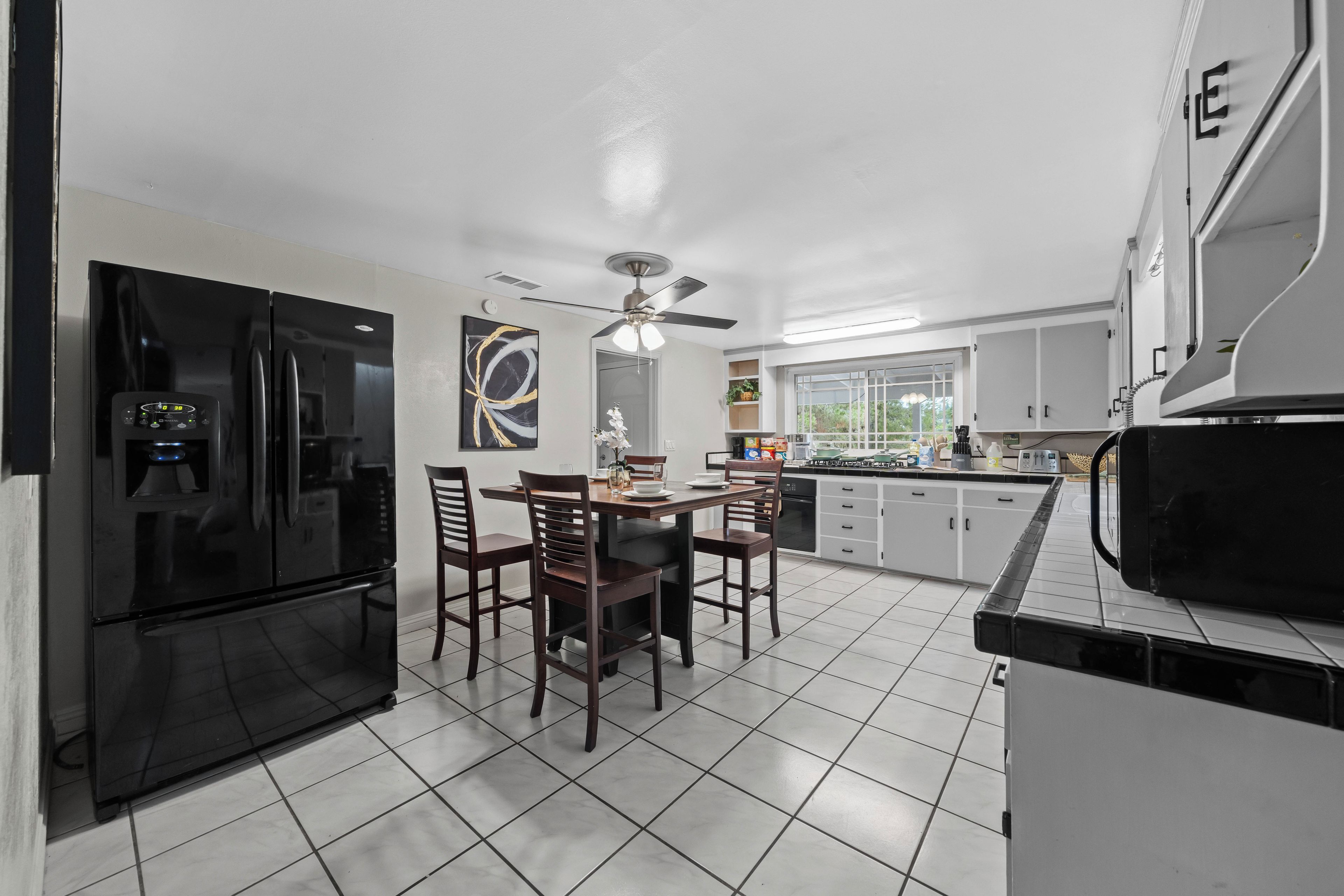 A modern kitchen with a black refrigerator, wooden dining table, and chairs.