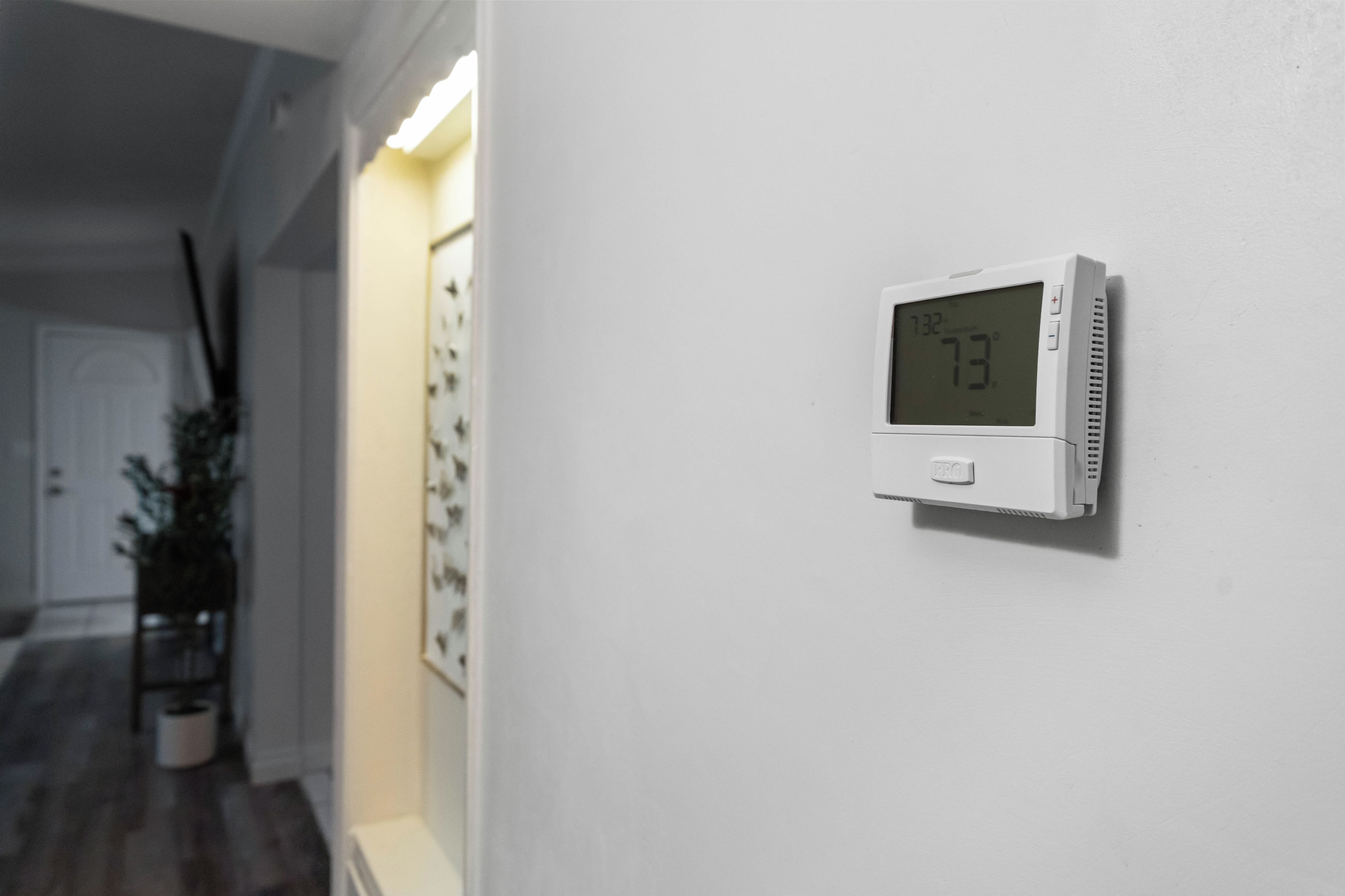 A thermostat on a white wall displaying a temperature of 73°F.