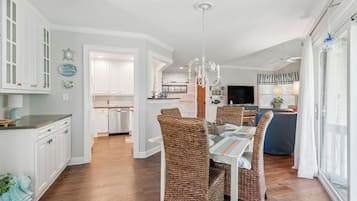 A spacious dining area with a high ceiling and a chandelier, leading to a kitchen and living area.