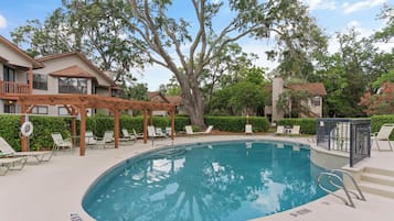 A pool area with lounge chairs, a pergola, and a view of a residential building.