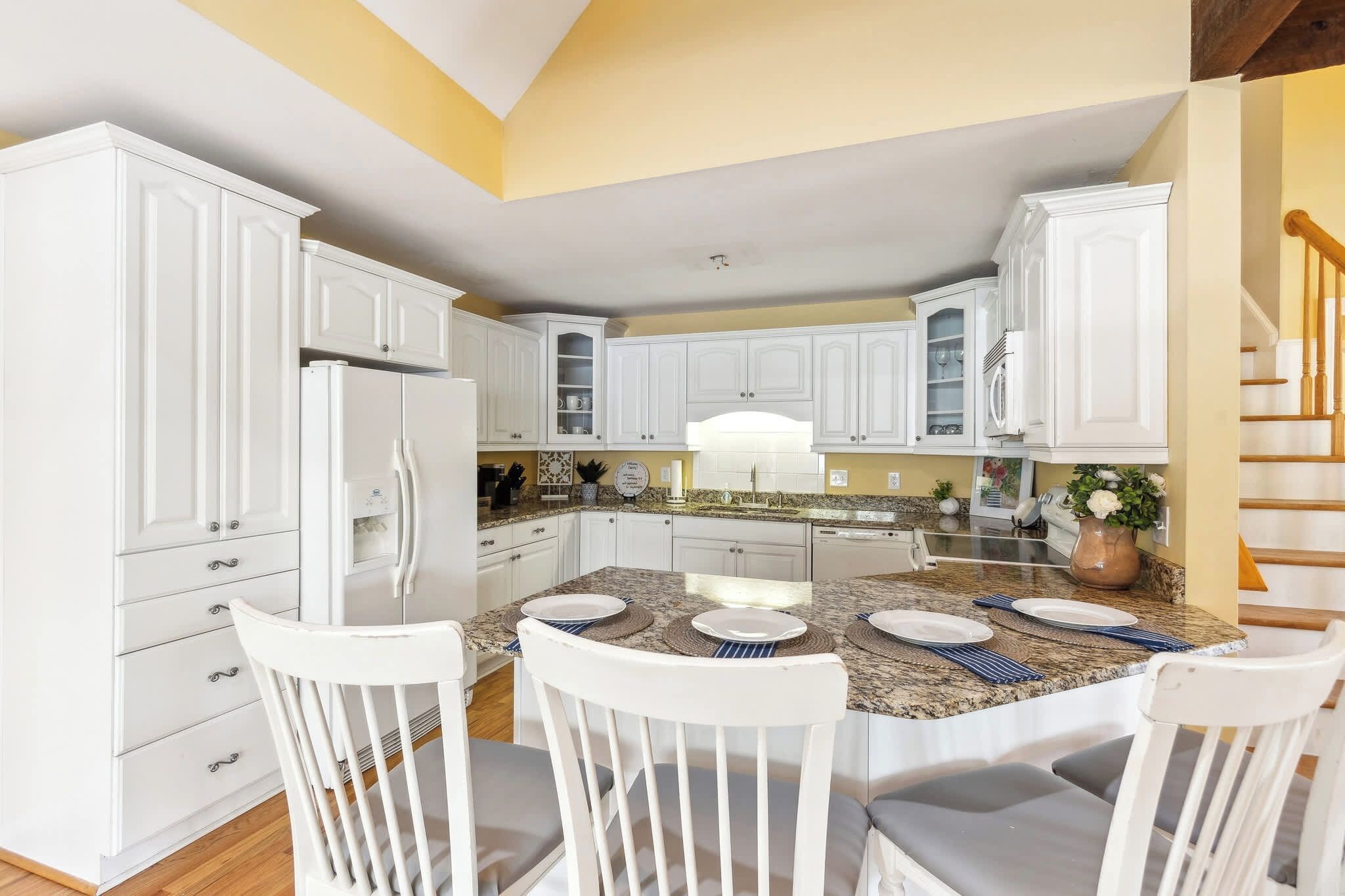 A modern kitchen with white cabinetry, granite countertops, and a dining area with white chairs and a table set for four.