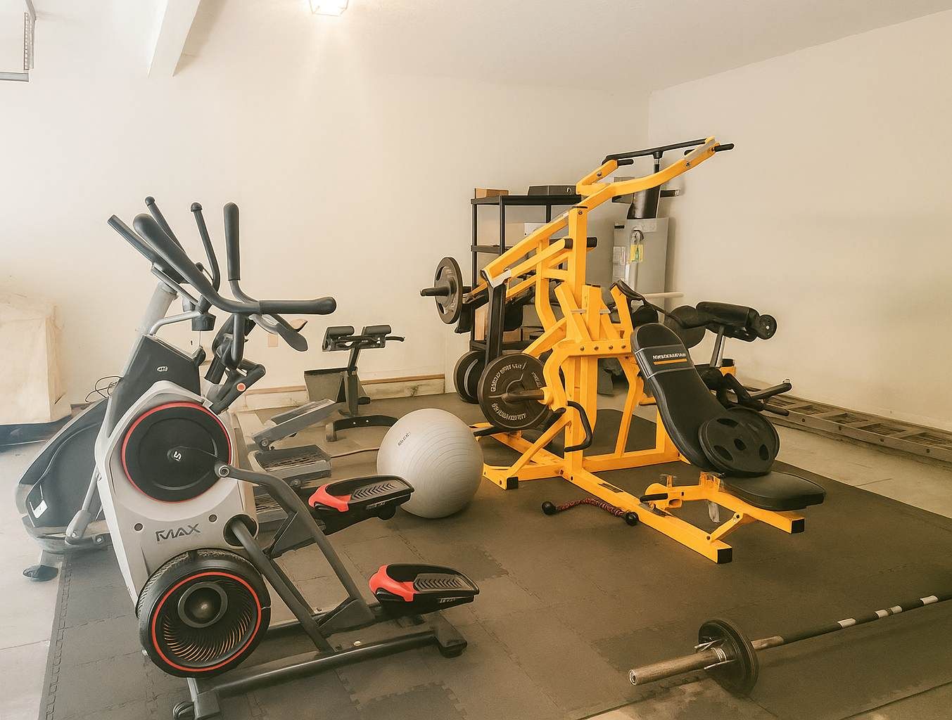 Un gimnasio con equipo de ejercicio, incluyendo una bicicleta estática, una máquina de remo, un banco de pesas y un banco para pesas.