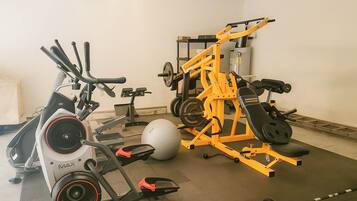 Un gimnasio con equipo de ejercicio, incluyendo una bicicleta estática, una máquina de remo, un banco de pesas y un banco para pesas.