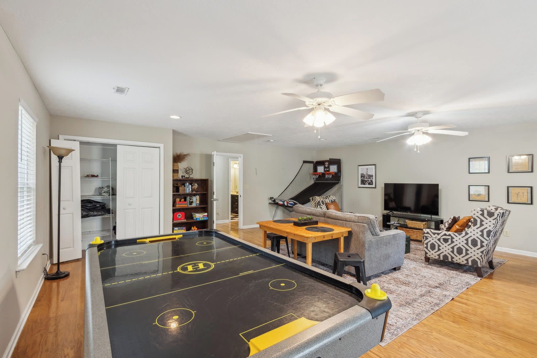 A living room with a shuffleboard table, a sofa, a television, and a ceiling fan.