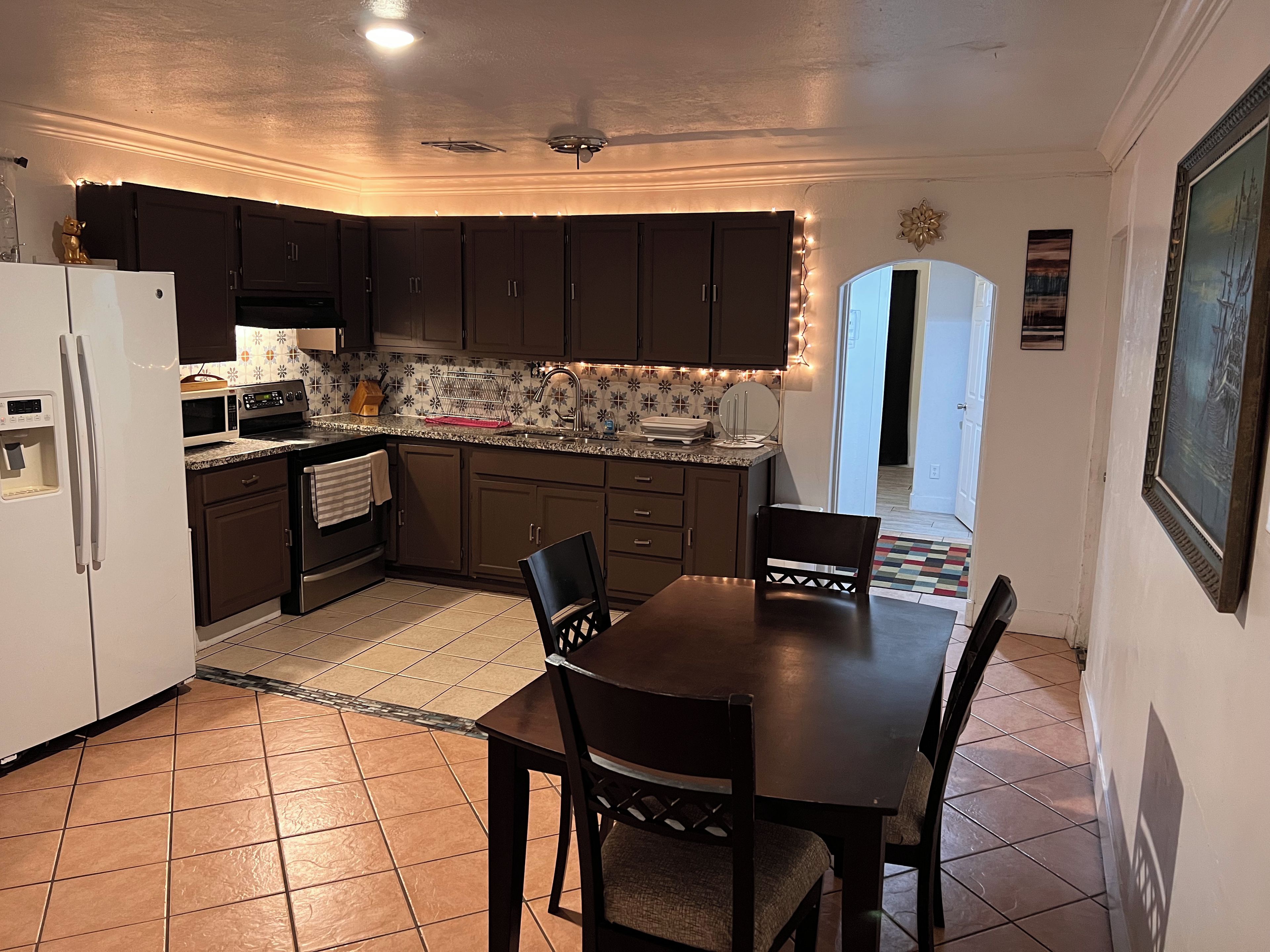 A kitchen with dark cabinets, a white refrigerator, a dining table with chairs, and a patterned backsplash.