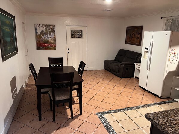 A compact living space with a dining table, chairs, a sofa, a refrigerator, and artwork on the walls.