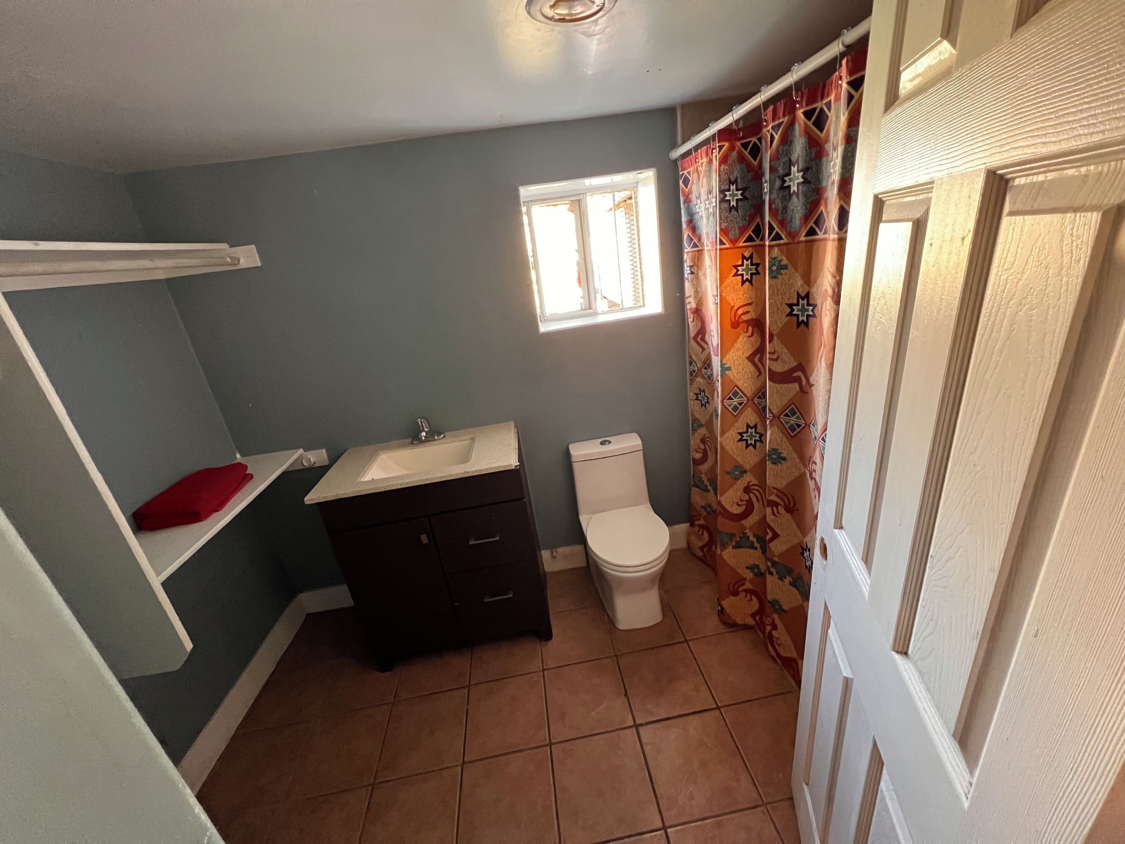 A bathroom with a white sink, dark cabinet, toilet, and a window.