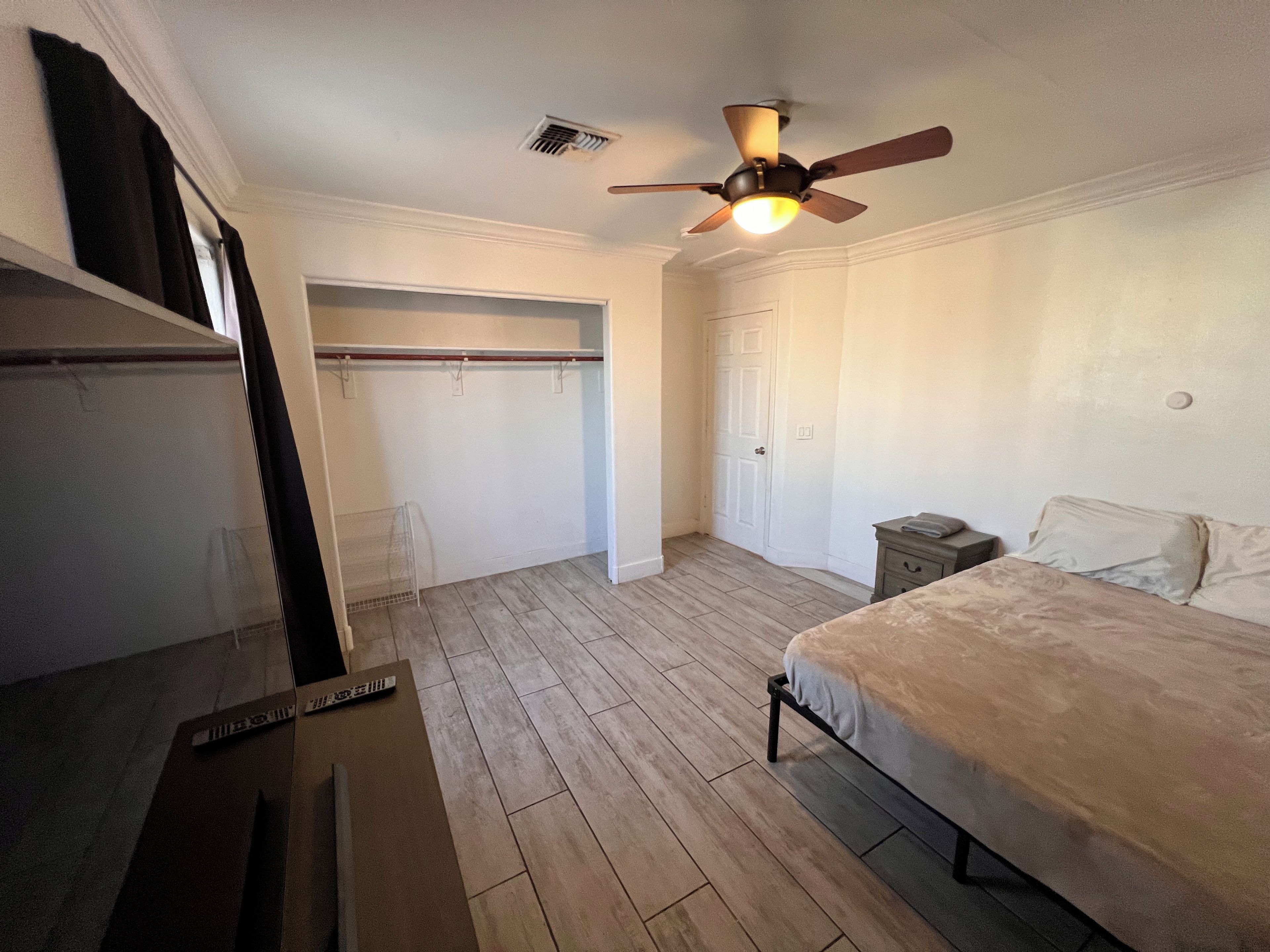Une chambre à coucher avec un lit, une table de chevet, un ventilateur de plafond, une porte et une fenêtre.