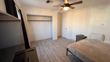 Une chambre à coucher avec un lit, une table de chevet, un ventilateur de plafond, une porte et une fenêtre.
