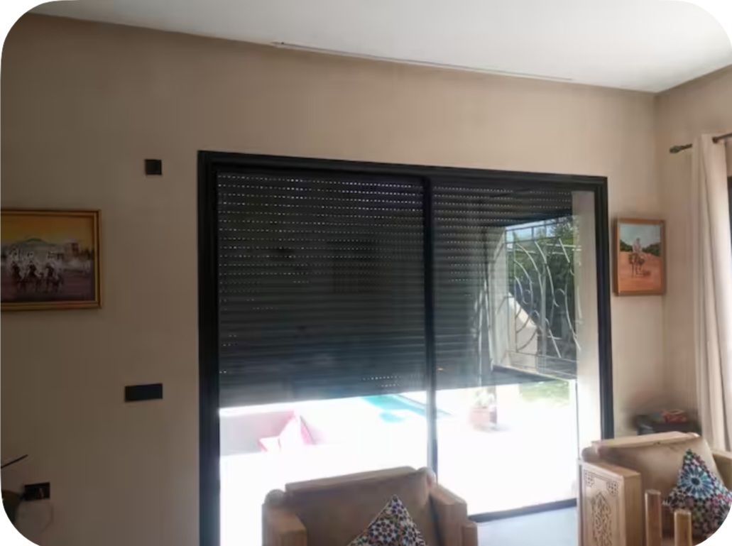 Una habitación con un gran ventanal corredero que da a un balcón, un cuadro en la pared y una silla con cojín estampado.