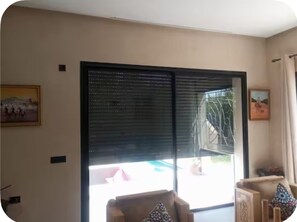 A room with a large sliding glass door leading to a balcony, a framed picture on the wall, and a chair with a patterned cushion. - New Listing (Marrakech)