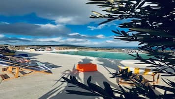 Zona junto a la piscina con sillones de descanso y un espacio de estar pequeño color naranja, con vista a una playa y el mar.