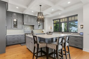 Une cuisine moderne avec des meubles gris, un grand îlot central doté de tabourets de bar et une fenêtre donnant sur la verdure.