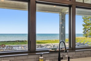 Une vue depuis une fenêtre donnant sur la mer et sur un espace verdoyant aménagé avec des chaises.