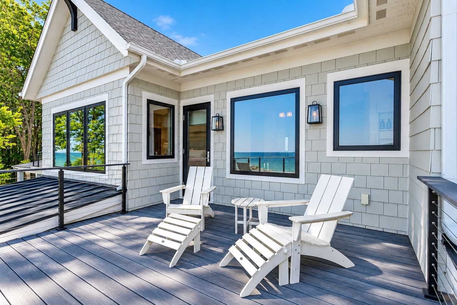 A modern house with a deck, large windows, and a view of the ocean.