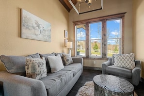 A living room with a grey sofa, a round coffee table, and a large window with a view of the outdoors. - Star of the Summit: 5 bedrooms, Private Indoor Pool, Stunning Views (Sevierville)