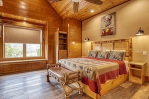 A wooden cabin bedroom with a large bed, a bench, a window, and a painting on the wall. - Tennessee Whiskey: Sweeping Views, Indoor Pool, 9-hole Golf (Sevierville)
