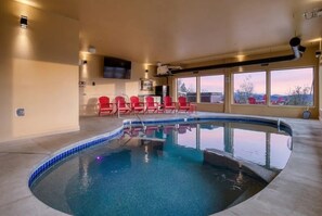 A swimming pool with a curved edge, surrounded by red chairs, and large windows offering a view of the outside. - Tennessee Whiskey: Sweeping Views, Indoor Pool, 9-hole Golf (Sevierville)