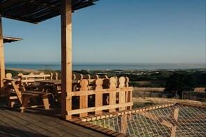 Una terraza de madera con mobiliario exterior, con vistas a un paisaje costero.