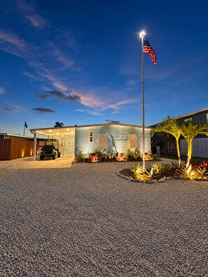 A two-story house with a garage, a flagpole with an American flag, and a driveway with a gravel surface. - Casita Azul - Pine Island Waterfront Retreat • Kayaks, Fishing & Outdoor Lounge (Saint James City)